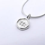 A silver-colored necklace with a round pendant featuring a zodiac sign symbol, attached to a chain.