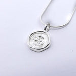 A silver pendant necklace with a round pendant featuring a star sign, attached to a chain.