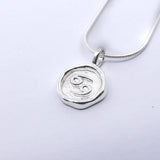 A silver pendant necklace with a round pendant featuring a star sign, attached to a chain.