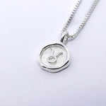 A silver necklace featuring a round pendant with a zodiac sign on it, attached to a delicate chain.