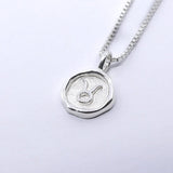 A silver necklace featuring a round pendant with a zodiac sign on it, attached to a delicate chain.