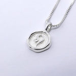 A silver necklace featuring a round pendant with a zodiac sign on it, attached to a delicate chain.
