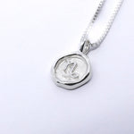 A silver necklace featuring a round pendant with a zodiac sign on it, attached to a delicate chain.