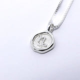 A silver necklace featuring a round pendant with a zodiac sign on it, attached to a delicate chain.