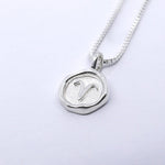 A silver necklace featuring a round pendant with a zodiac sign on it, attached to a delicate chain.