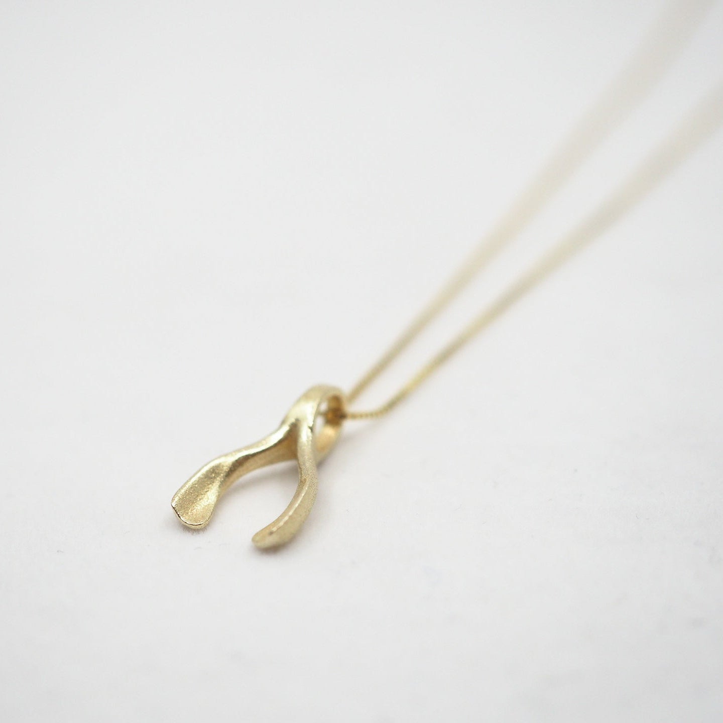 A gold wishbone pendant necklace on a delicate gold chain, photographed on a clean white background.