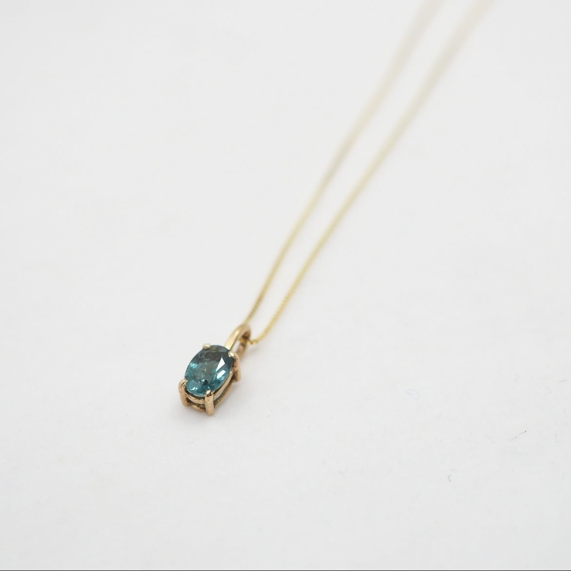 Gold necklace with a blue gemstone pendant on a white background