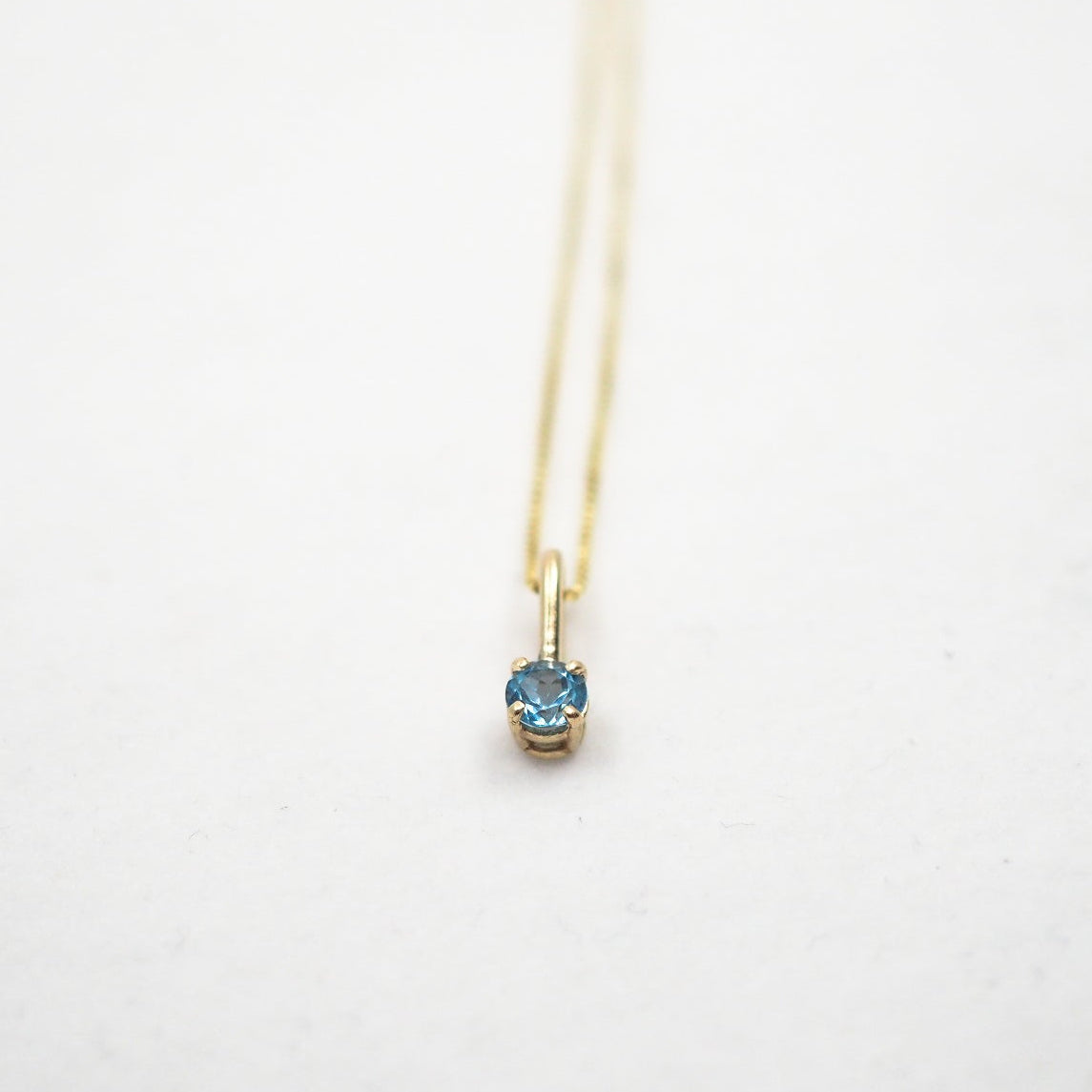 Gold necklace with a blue gemstone pendant on a white background