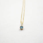 Gold necklace with a blue gemstone pendant on a white background