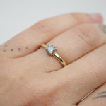 Gold ring with a diamond on a person's finger against a white background