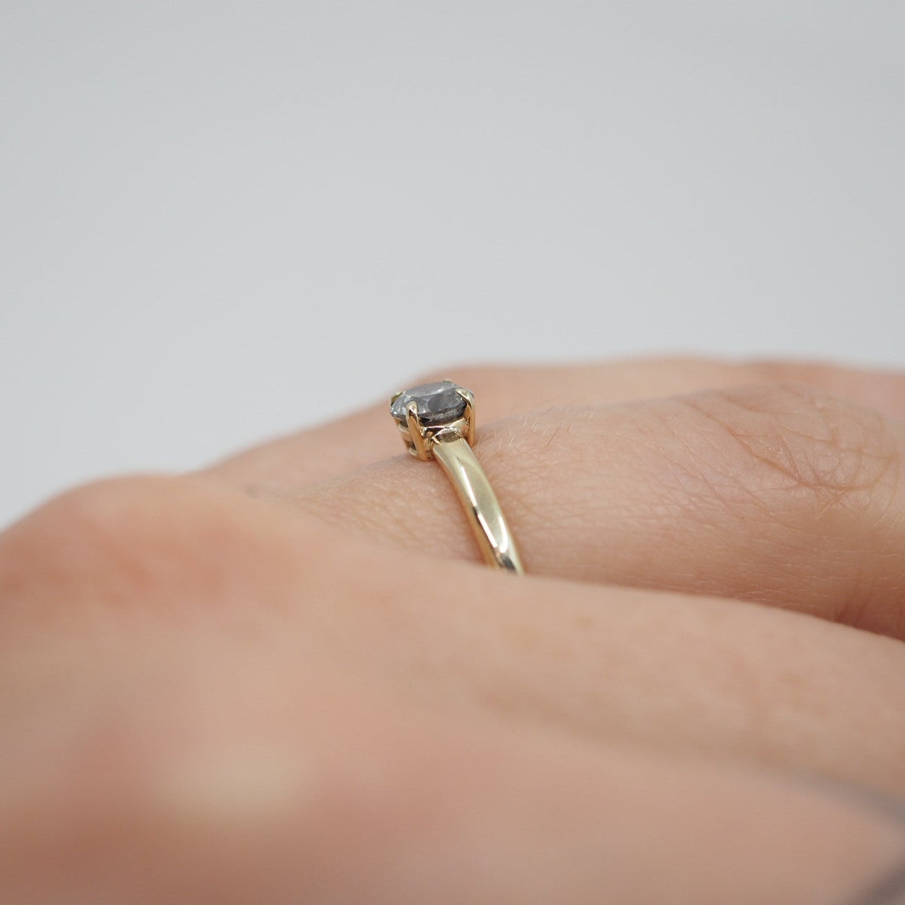 Gold ring with a diamond on a person's finger against a neutral background
