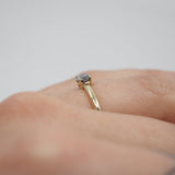 Gold ring with a diamond on a person's finger against a neutral background