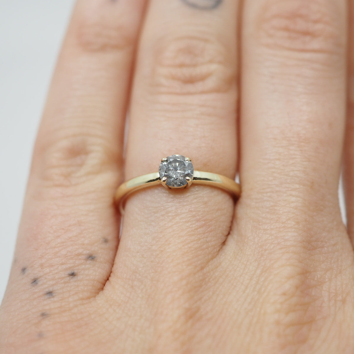 Gold ring with a diamond on a person's finger against a neutral background
