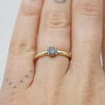 Gold ring with a diamond on a person's finger against a neutral background