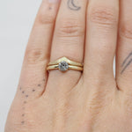 Two gold rings on a person's finger against a light background. One ring with a diamond and the other ring in a chevron shape.