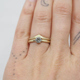 Two gold rings on a person's finger against a light background. One ring with a diamond and the other ring in a chevron shape.
