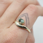 Gold ring with a green gemstone on a finger with a tattoo.