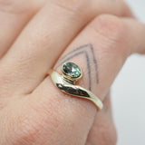 Gold ring with a green gemstone on a finger with a tattoo.