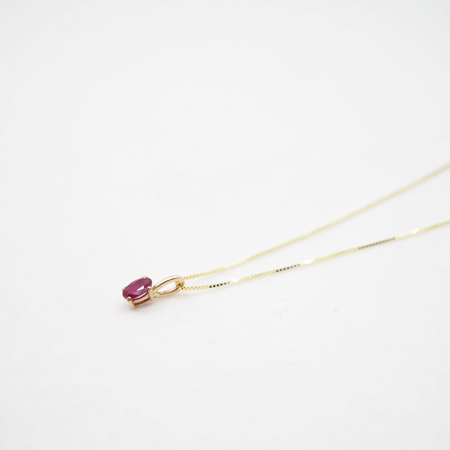 Gold necklace with a small pink gemstone on a white background