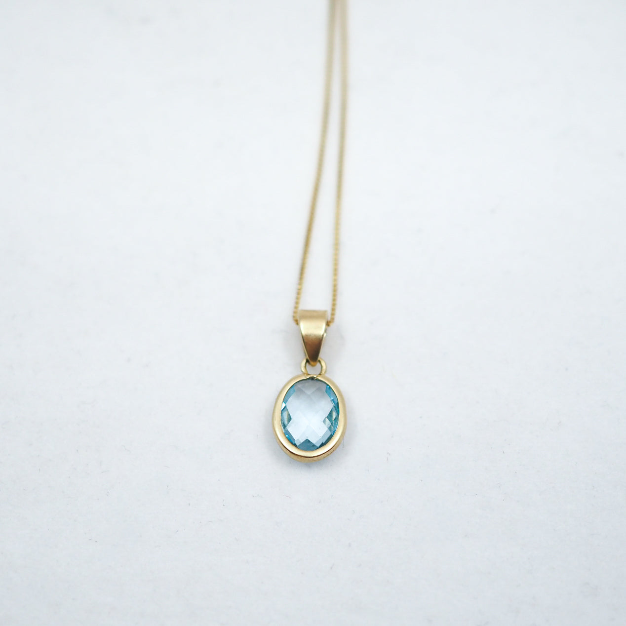 Gold necklace with a blue gemstone pendant on a light gray background