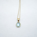 Gold necklace with a blue gemstone pendant on a light gray background