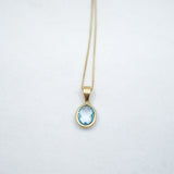Gold necklace with a blue gemstone pendant on a light gray background