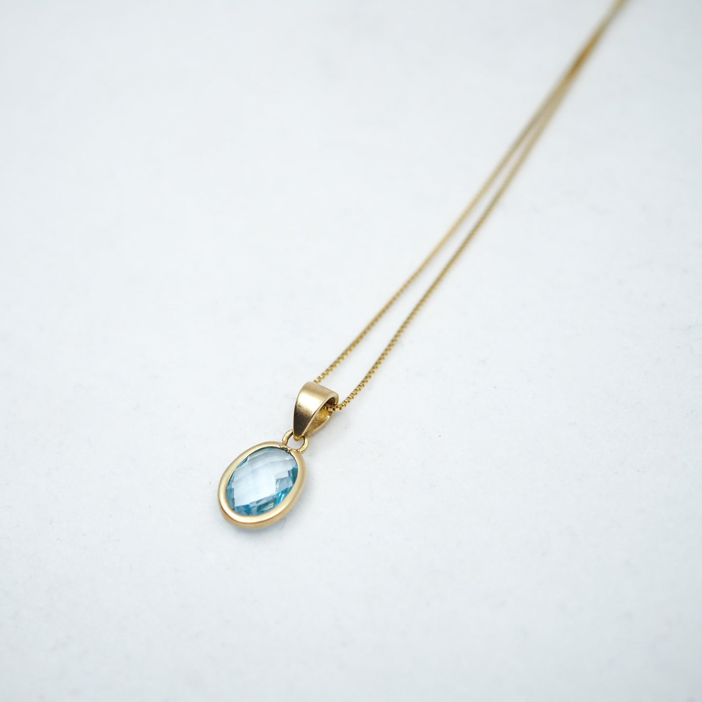 Gold necklace with a blue topaz gemstone pendant on a white background