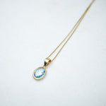Gold necklace with a blue topaz gemstone pendant on a white background