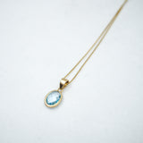 Gold necklace with a blue topaz gemstone pendant on a white background