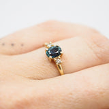 Gold ring with a blue gemstone on a person's finger against a neutral background