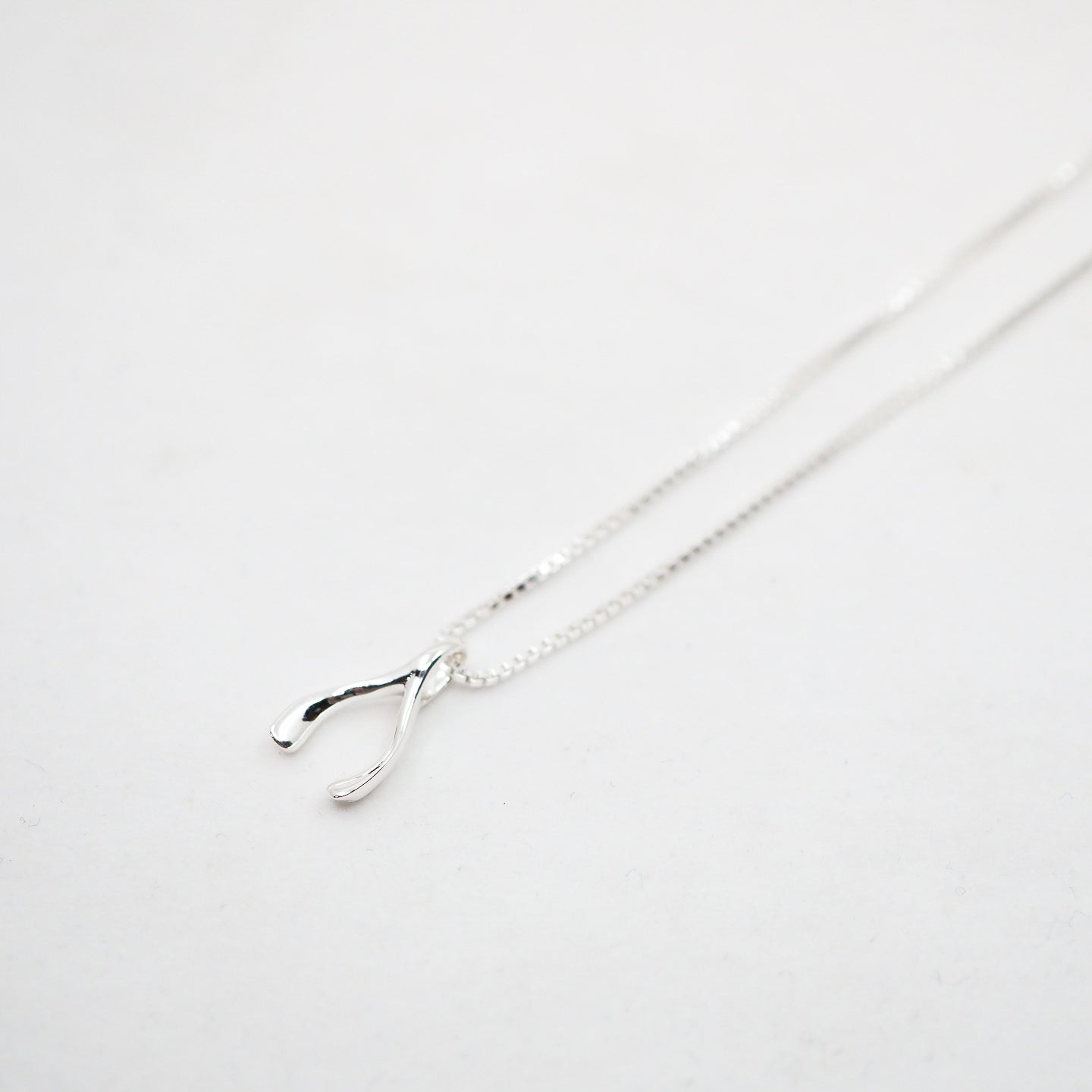 Silver necklace with a wishbone pendant on a light gray background