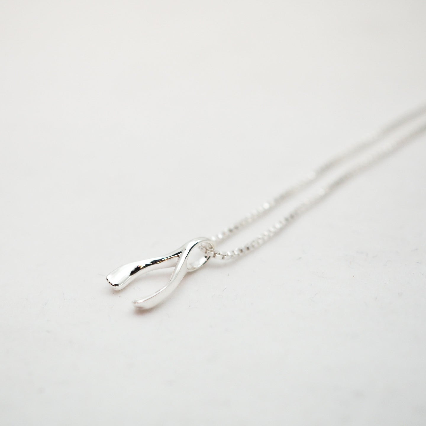 Silver necklace in the shape of a wishbone on a light gray background