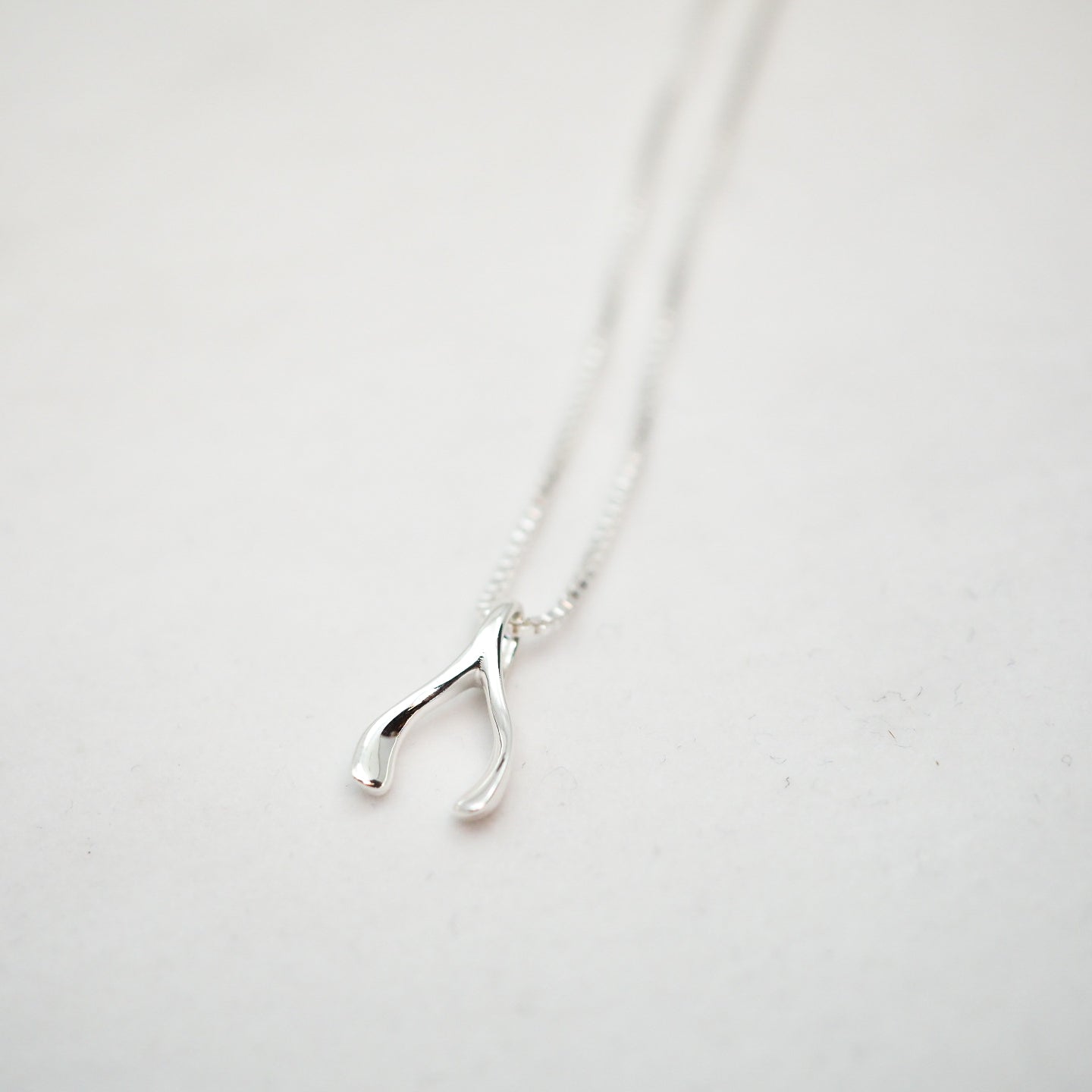 Silver wishbone pendant necklace on a white background