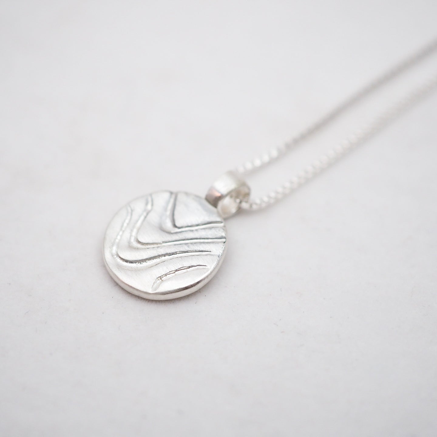 Silver necklace with a round pendant on a light gray background
