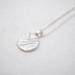 Silver necklace with a round pendant on a light gray background