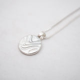 Silver necklace with a round pendant on a light gray background