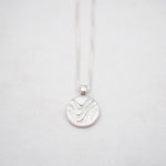 Silver necklace with a round pendant on a light gray background