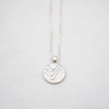 Silver necklace with a round pendant on a light gray background