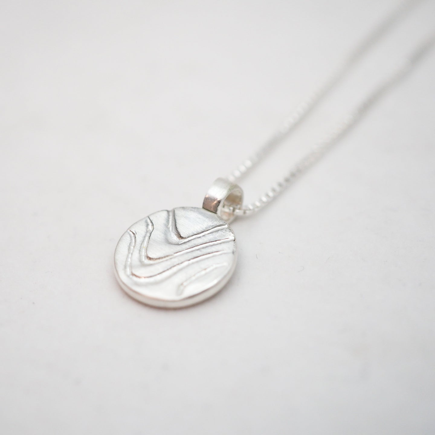 Silver necklace with a round pendant on a light gray background