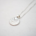Silver necklace with a round pendant on a light gray background