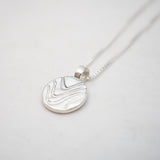 Silver necklace with a round pendant on a light gray background