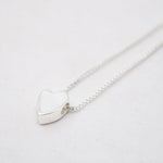 Silver heart-shaped pendant on a chain against a light gray background