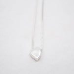Silver heart-shaped pendant on a white chain against a light gray background