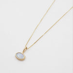 Gold necklace with a round pendant on a light gray background
