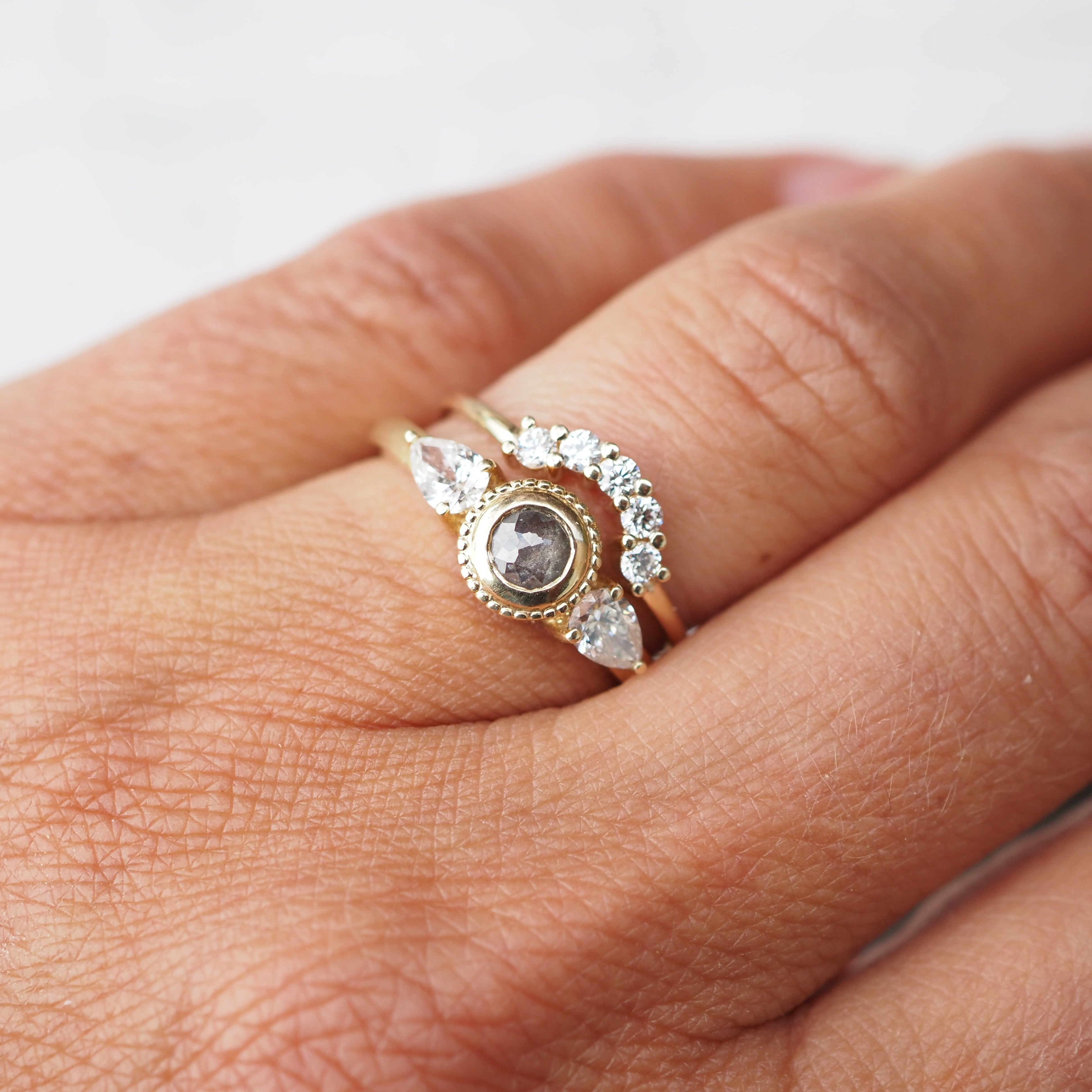 Gold ring with a central gemstone and smaller stones on a finger against a neutral background