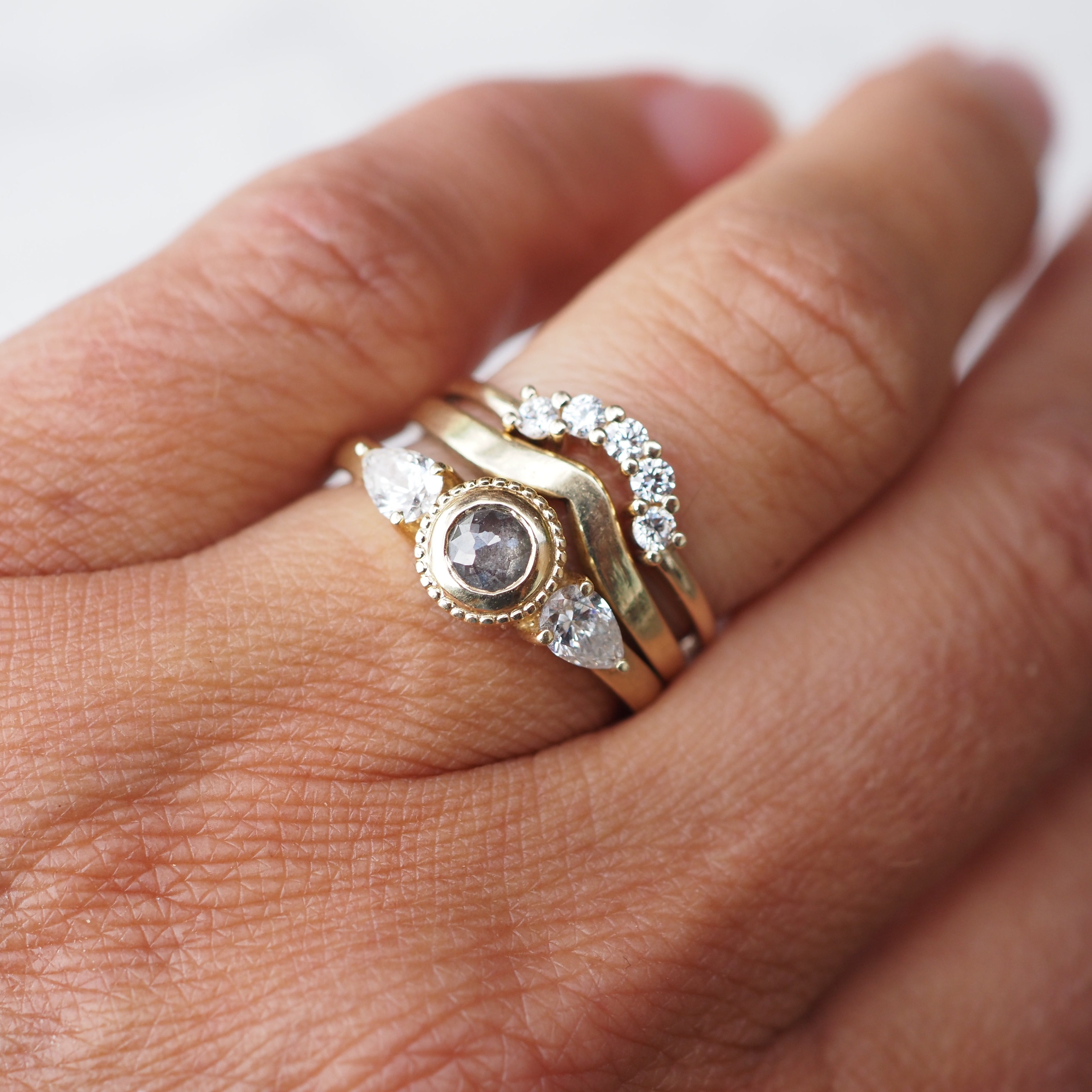 Hand wearing a gold ring with a central gemstone and diamond accents on a white background