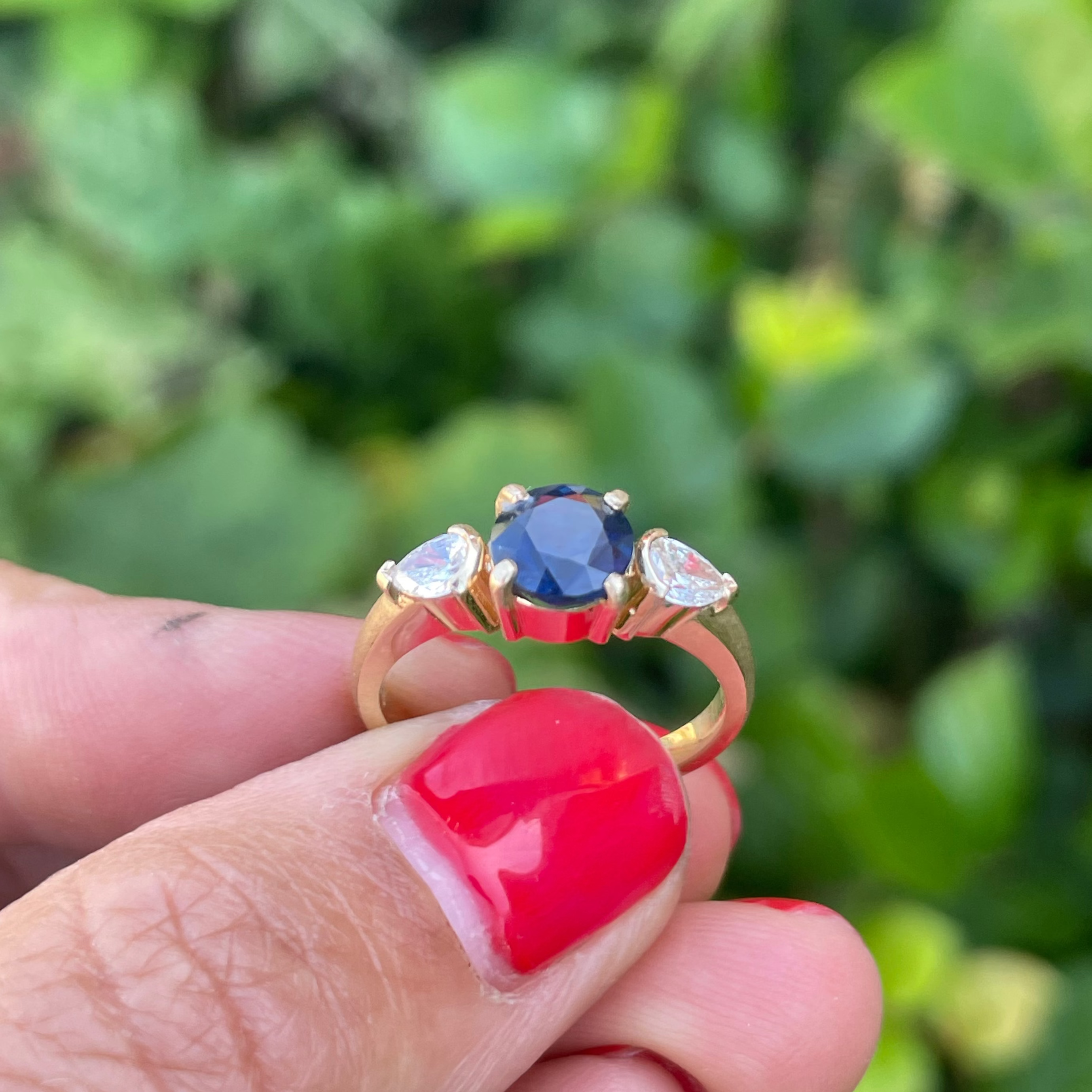 Gold ring with a blue gemstone held by a hand against a blurred green background