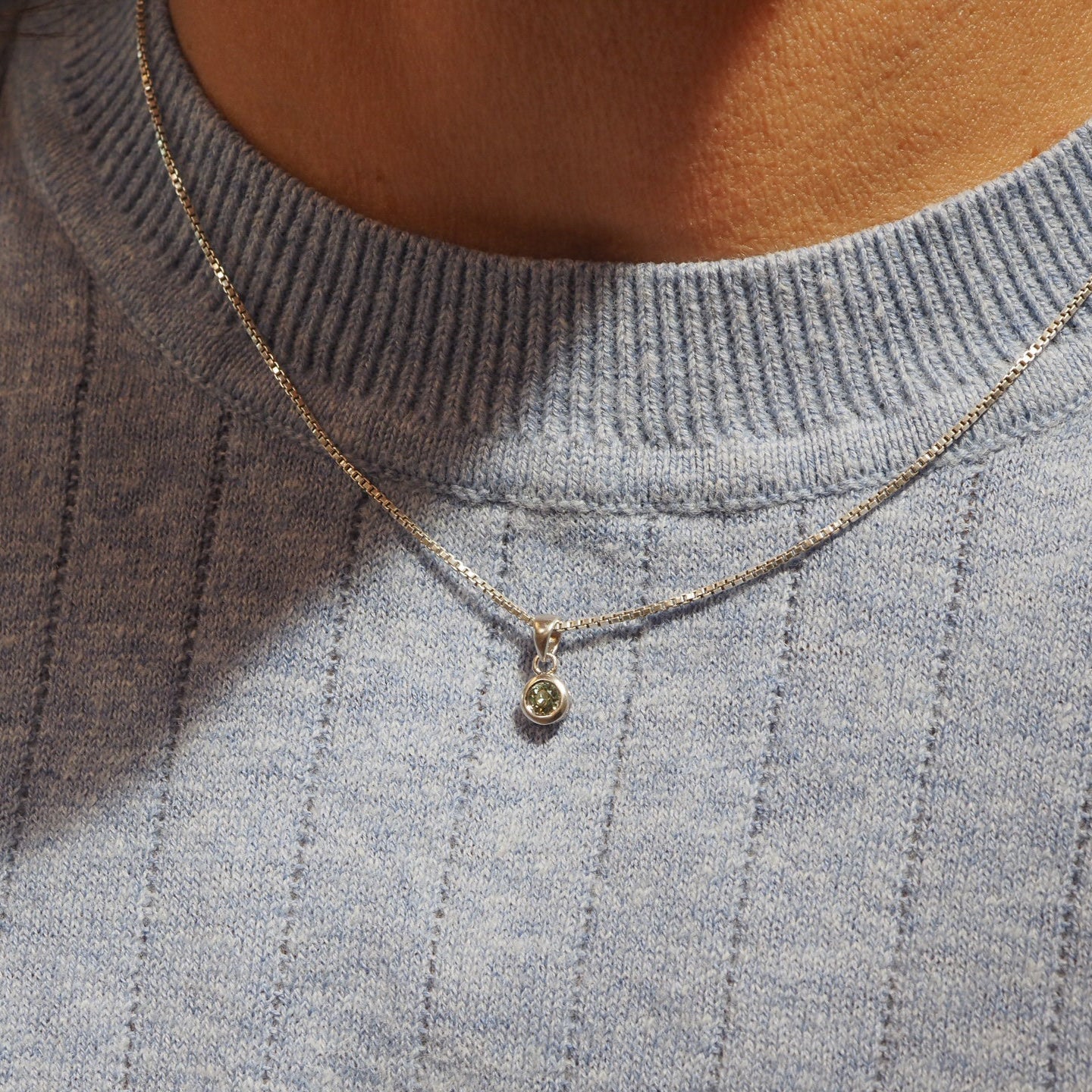 Necklace with a pendant on a person wearing a gray sweater