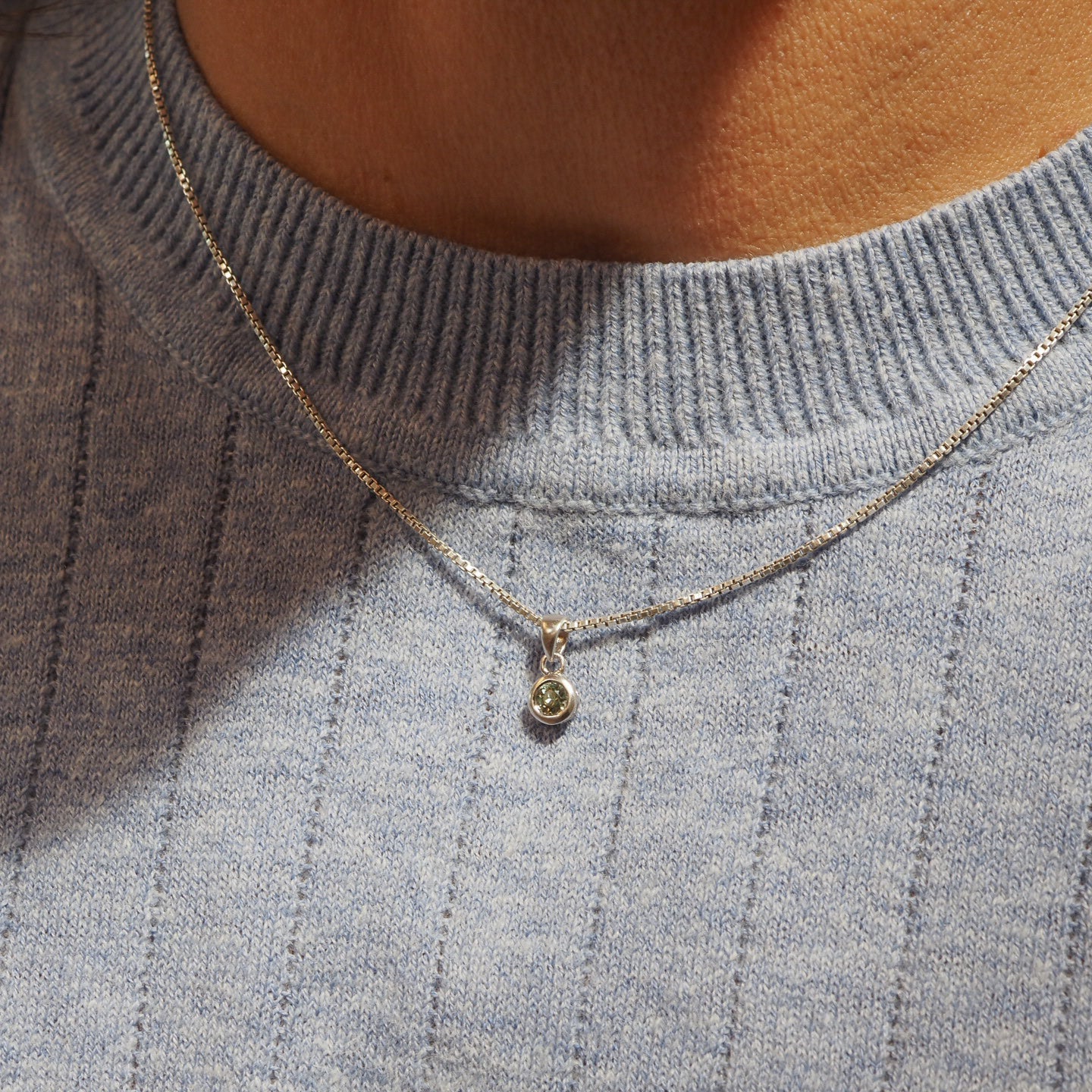 Necklace with a pendant on a person wearing a gray sweater