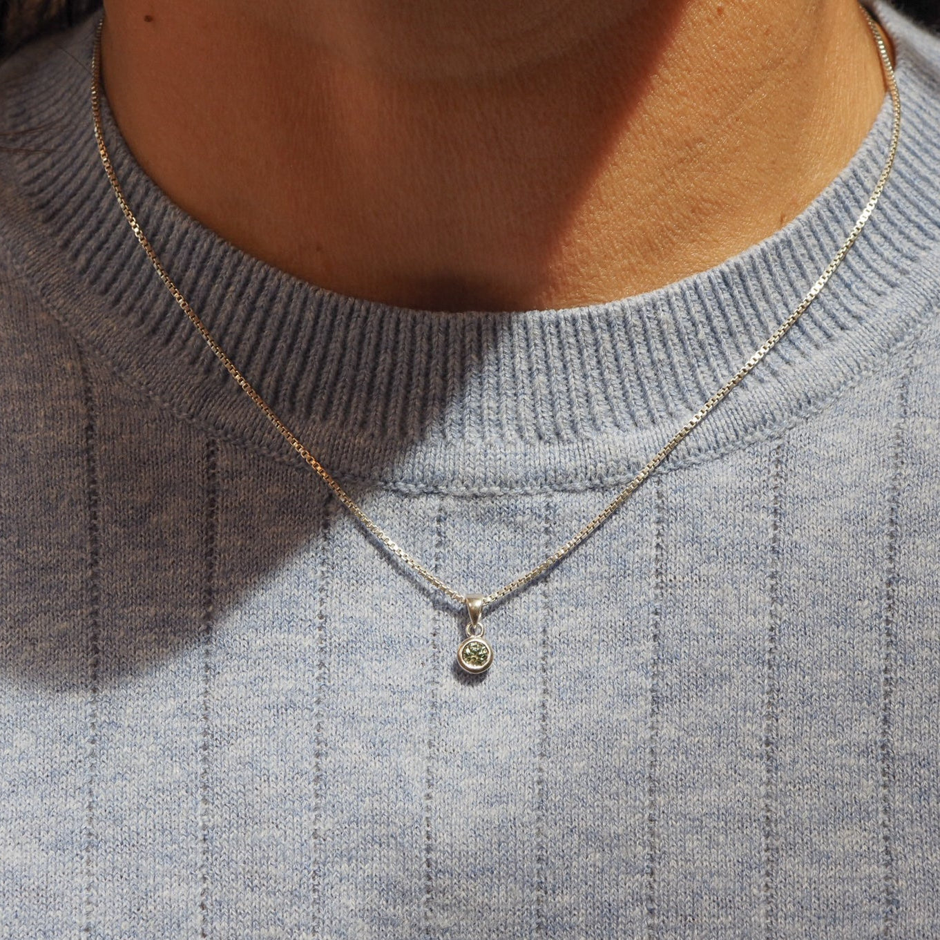 Necklace with a small pendant worn by a person in a gray sweater.